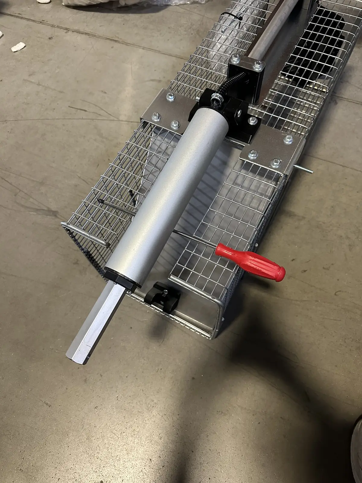 The motor lying along the top of the cage, propped up with a red-handled tool